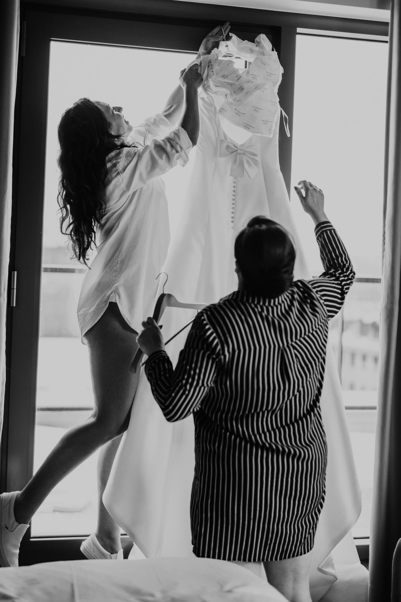 Bride hangs dress while bridesmaid helps