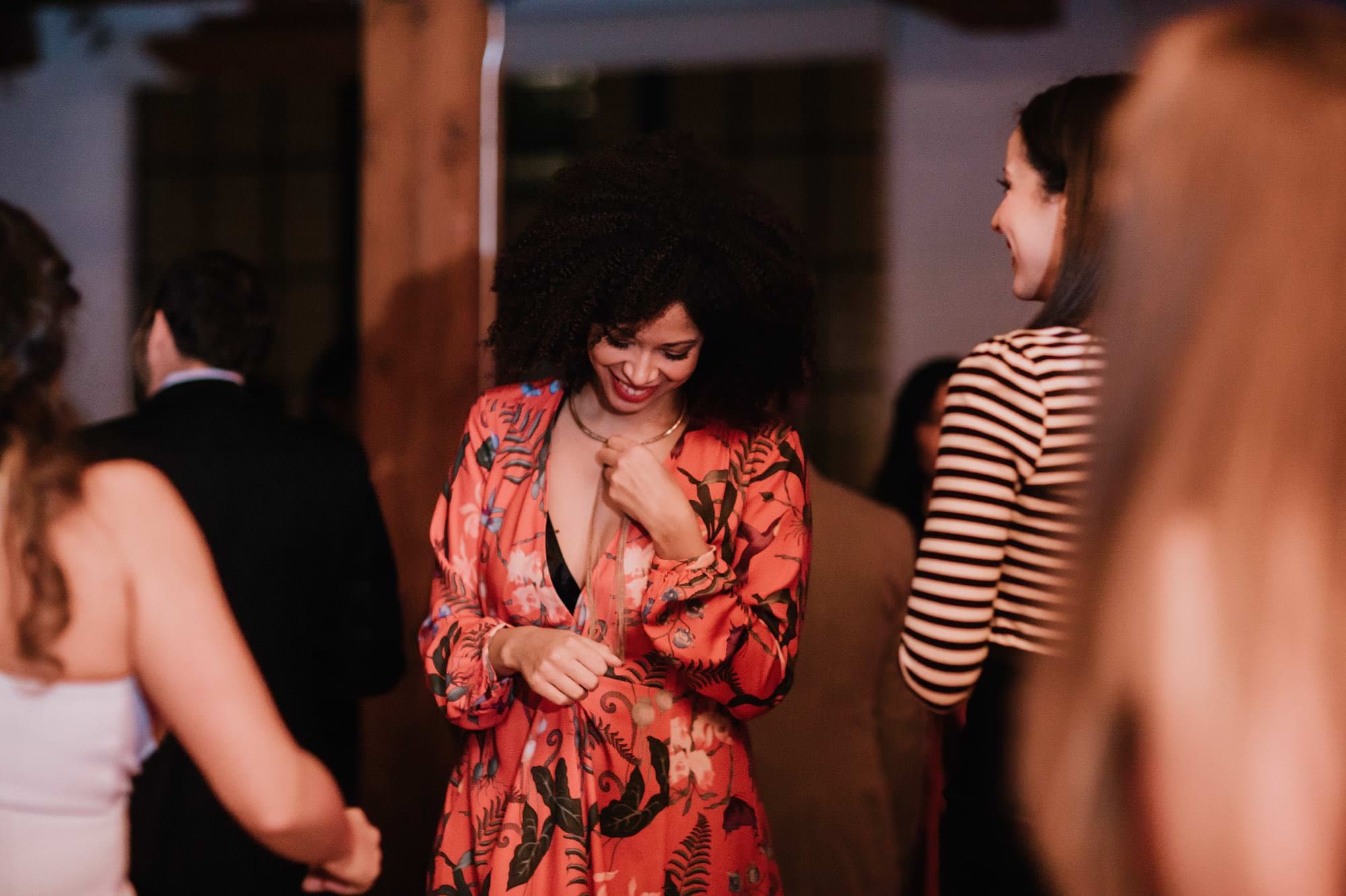A guest with curly hair in a red dress looks down candidly while dancing