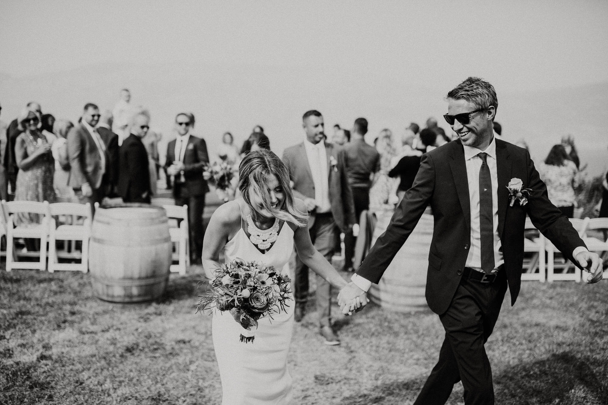 Black and white photo of bride and groom walking down the aisle at Evolve Cellars Vineyard on Lake Okanagan, Summerland, BC. Destination wedding photographer Brent Calis.