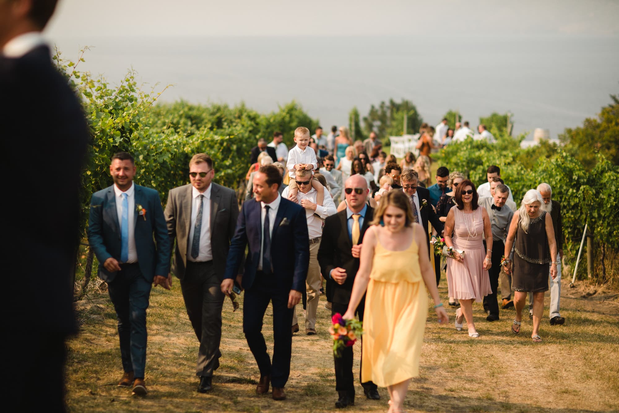 Wedding guests leave the ceremony at Evolve Cellars Vineyard on Lake Okanagan, Summerland, BC. Destination wedding photographer Brent Calis.