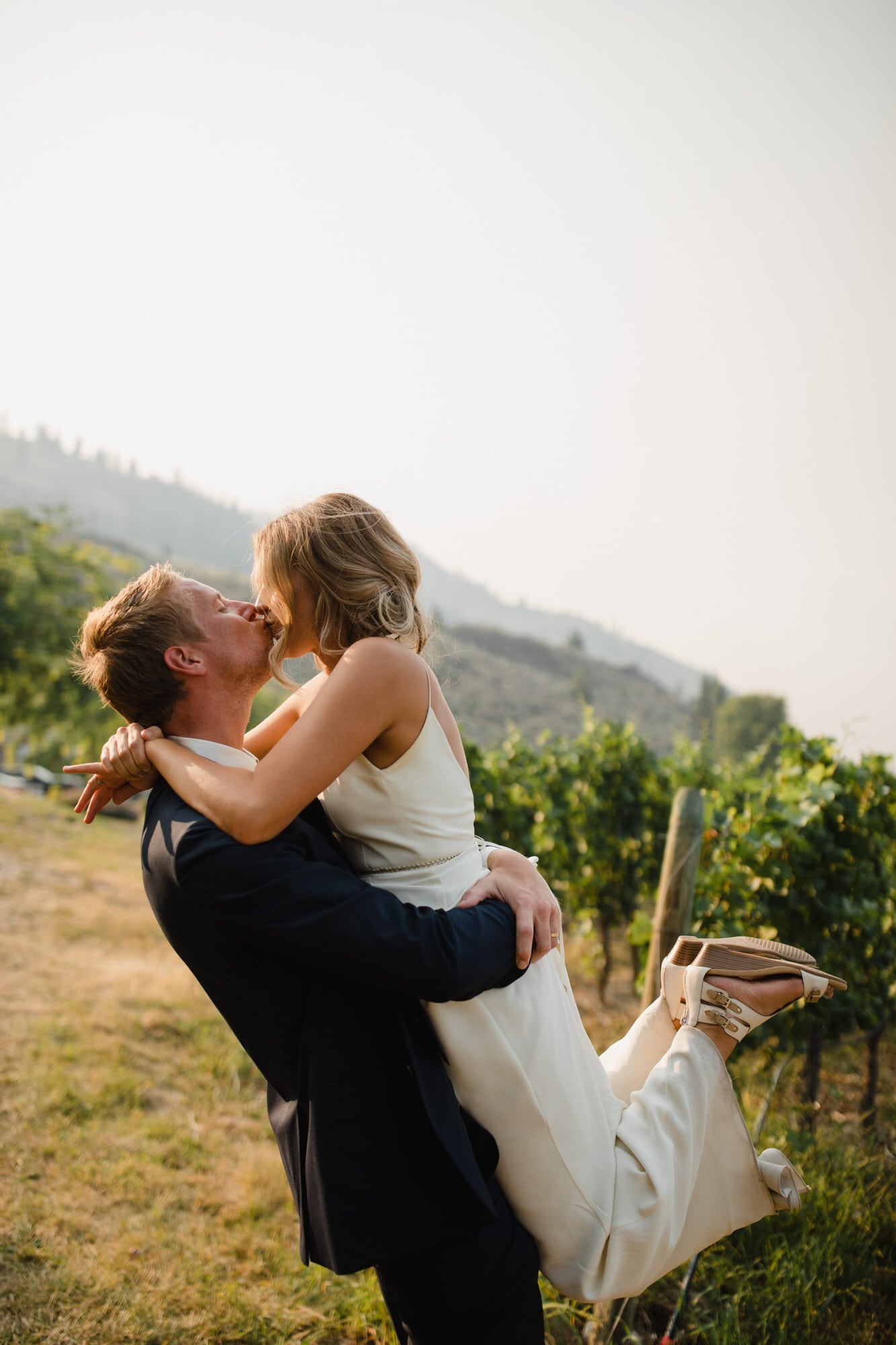 Groom lifts the bride for a kiss at Evolve Cellars Vineyard on Lake Okanagan, Summerland, BC. Destination wedding photographer Brent Calis.